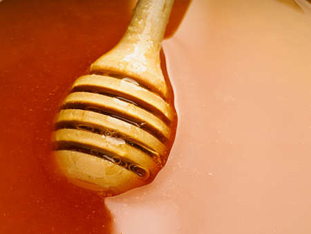 Wooden spoon on surface of honey. Reflection and play of light on honey surface. Close-up view. Macro shotの写真素材