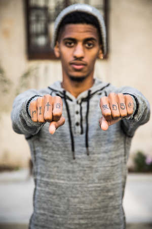 A portrait of a young, black man showing off the tattoos on the knuckles of his hands. Model Released and shot during the autumn of 2016.の写真素材