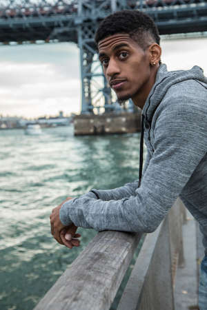 A young man sits and admires the view of NYC's Williamsburg Bridge. Shot during the Autumn of 2016 in Brooklyn, New York City.の写真素材