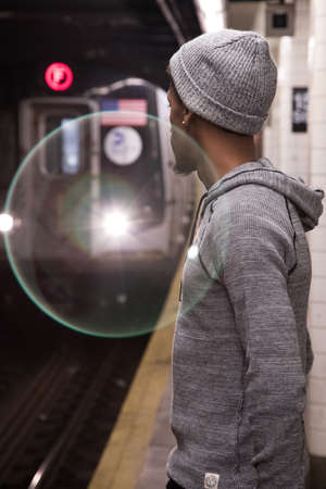 A young, black male waits for a New York City subway train. Shot during the autumn of 2016.