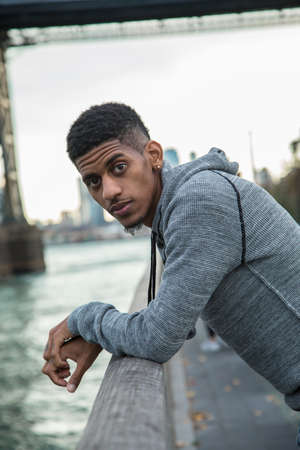 A portrait of a young, black man, pensively standing along New York City's East River and Williamsburg Bridge.の写真素材