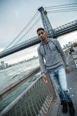 A portrait of a young, black man, pensively standing along New York City's East River and Williamsburg Bridge.の写真素材