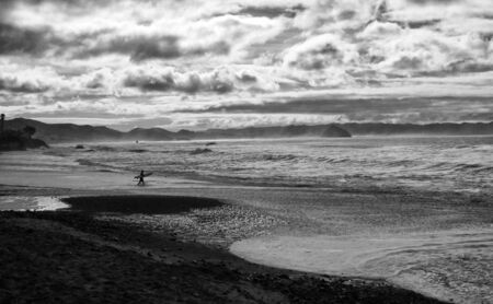 Conceptual Abstract Black and White of Lone Surfer Entering Vast Coastline with Cloudy Skies in Contrastの写真素材
