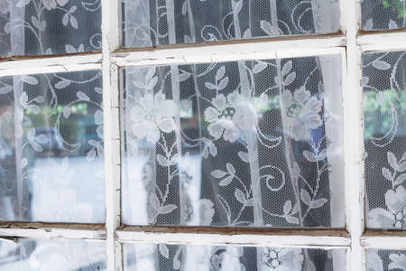 Lace Curtains Hang Behind Glass with Peeling White Wooden Frameの写真素材