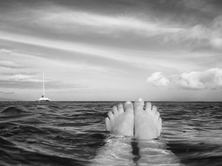 Black and white image toes floating in ocean with boat on horizonの写真素材