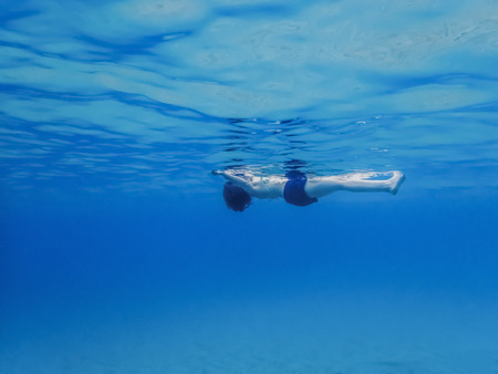 Woman floating on surface of blue ocean low angle underwater imageの写真素材