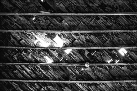 Ceiling with wood shingles eroding and falling away and strong rustic lines.  Black and white image...