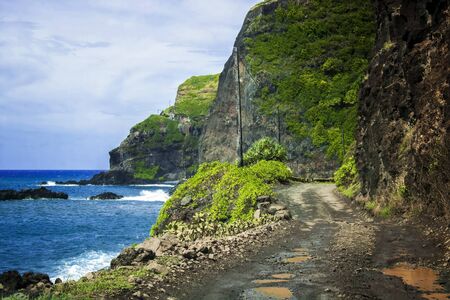 Dirt and gravel road winds along between sea and cliffs in Hawaii.の写真素材