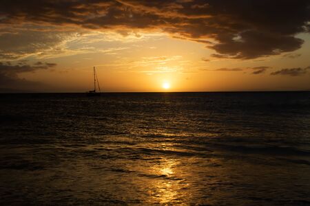 Sunset seascape with boat on horizon under orange sky reflecting on surface of Pacific.の写真素材