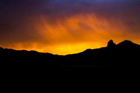 Vivid sunset through rain band and clouds over black mountain silhouette on horizon.  Desert sunset from Arizona.の写真素材