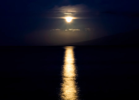 Full moon dropping through clouds and setting over ocean with light glowing on surface of the sea in Hawaii.の写真素材