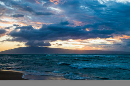 Pastel sunset with cloud filled sky over stormy windblown sea with island on horizon.