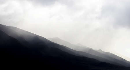 Black and white mountain ridgelines beneath clouds lead across bottom of image for graphic dramatic background.の写真素材