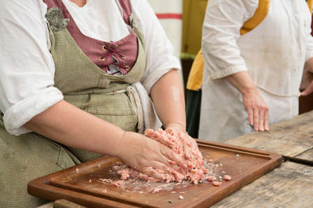 A woman dressed in Renaissance era costume makes sausage with her hands on a cutting board.の写真素材