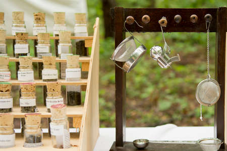 Tea in glass tubes in a display stand and tea strainers hanging from wooden pegs on display for sale at a fair.の写真素材