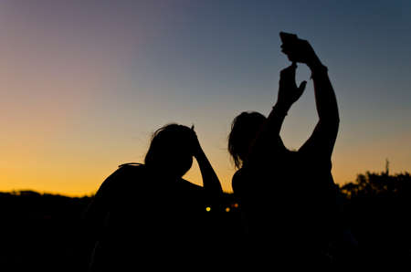 silhouette of two people taking a picture at duskの写真素材