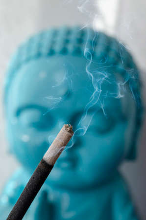 Smoking incense stick with buddha statue in the background