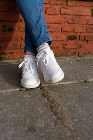 Woman legs with white leather sneakers.