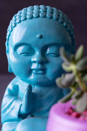 Turquoise Buddha statue with plant in front. Dark background. Pink flowerpot.の写真素材
