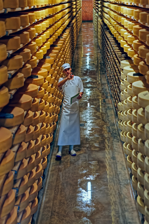 GRUYERE, SWITZERLAND - DECEMBER 31, 2014: Gruyere cheese factory worker in a cellar of the Maison du Gruyere (cheese dairy) in Switzerland. Gruyere is a famous swiss cheeseのeditorial素材