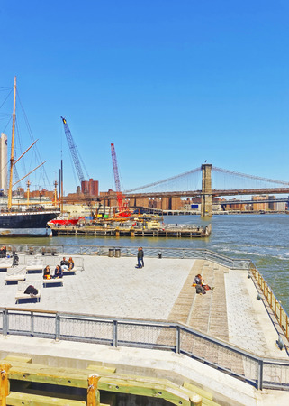 NEW YORK, USA - APRIL 25, 2015: Tourists relaxing on sunbeds in Pier in Manhattan, New York. View from Ferry on Pier in South Street Seaport. Brooklyn Bridge and Manhattan Bridge on the background.のeditorial素材