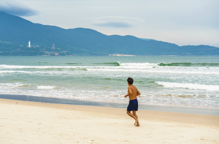 Man running near the China Beach in Danang in Vietnam. It is also called Non Nuoc Beach. South China Sea and Marble Mountains on the background.の写真素材