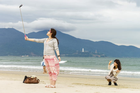 Danang, Vietnam - February 20, 2016: Young girls making a selfie with selfie stick at the China Beach in Danang in Vietnamのeditorial素材