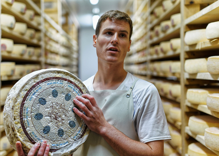Evillers, France - August 31, 2016: Cheesemaker holding a wheel of Comte Cheese in ripening cellar at Franche Comte creamery, in Franceのeditorial素材