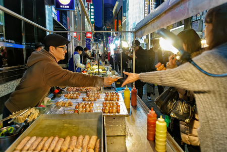 Seoul, South Korea - March 14, 2016: Girl buying food from the street trader at Myeongdong open street market in Seoul, South Korea. Selective focusのeditorial素材