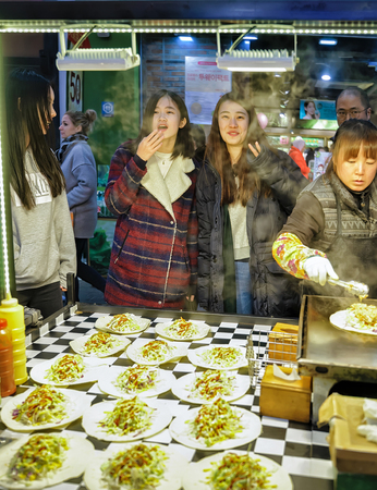 Seoul, South Korea - March 14, 2016: Seller and young buyers of street food in Myeongdong open street market in Seoul, South Koreaのeditorial素材