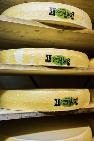 Pile of aging Gruyere de Comte Cheese on wooden shelves in ripening cellar of Franche Comte dairy,...