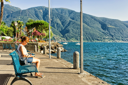 Ascona, Switzerland - August 23, 2016: Woman sitting on the bench at the embankment of the expensive resort in Ascona on Lake Maggiore, Ticino canton, Switzerland.のeditorial素材