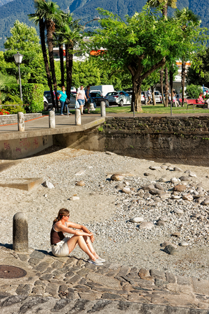 Ascona, Switzerland - August 23, 2016: Woman sitting on the shore at the embankment of the expensive resort at Ascona on Lake Maggiore, Ticino canton, Switzerland.のeditorial素材