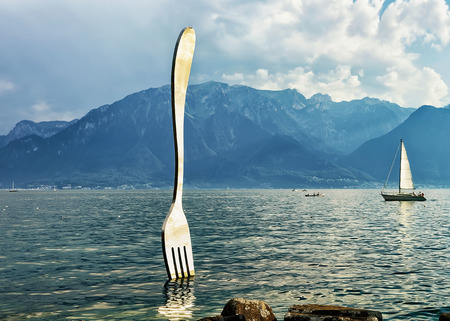 Vevey, Switzerland - August 27, 2016: Fork sculpture at Geneva Lake in Vevey, Vaud canton, Switzerland. Sailing ship and Alps mountains on the backgroundのeditorial素材