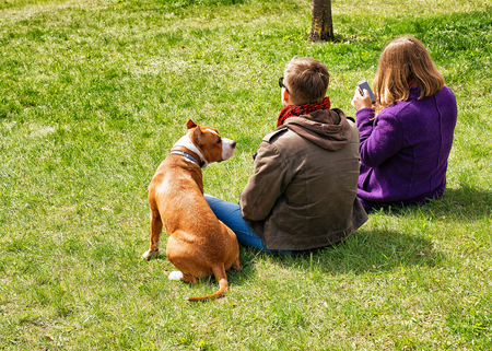 Vilnius, Lithuania - April 30, 2016: Young couple with their boxer dog sitting on the green lawn in springのeditorial素材
