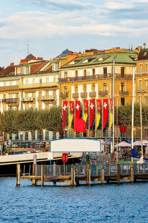 Sunset at Pier with Swiss flags on Geneva Lake near Promenade du Lac in summer, Geneva, Switzerland. People on the backgroundの写真素材
