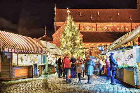 Riga, Latvia - December 26, 2015: People enjoy hot drinks near the Christmas tree at the market in old Riga, Latvia. At Christmas market. Motion blur. Selective focus.のeditorial素材
