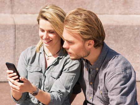 Young girl looking at mobile phone with her boyfriend with interest as friendship and togetherness conceptの写真素材
