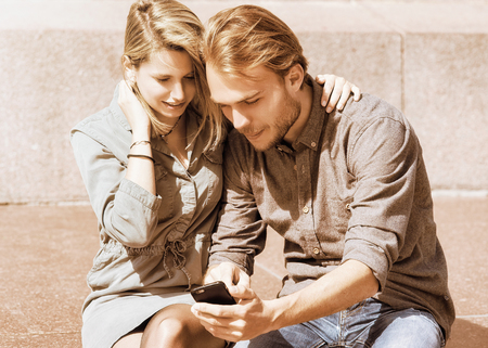 Young girl looking at mobile phone of her boyfriend with interest and surprise as friendship and togetherness conceptの写真素材