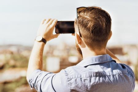 Young caucasian man taking photos on his mobile phoneの写真素材
