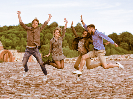 Group of smiling young multiracial friends trying to jump up simultaneously as fun togetherness activity conceptの写真素材