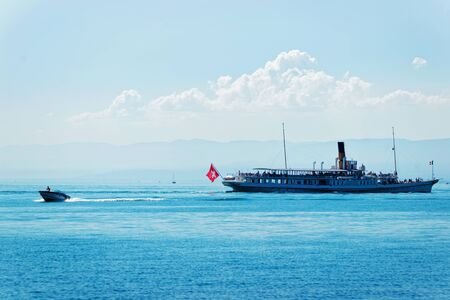 Water ferry with Swiss flag on Lake Geneva at Ouchy embankment in Lausanne, Switzerland. People aboardの写真素材