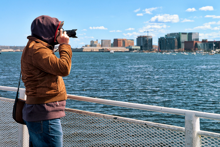 Man with camera at Charles river with the skyline of the city in the background in Boston, Americaの写真素材