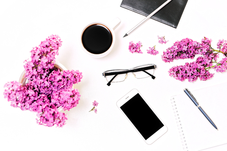 Workplace with mobile phone, notebook, pencil, pen, glasses and lilac flowers on the white table background. Flat lay, top viewの写真素材
