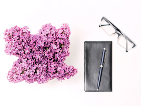 Working place with diary, pen, glasses and lilac flowers on the white table background. Flat lay, top viewの写真素材