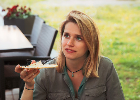 Young woman eating pizza in a street cafeの写真素材
