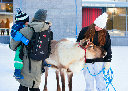 Rovaniemi, Finland - March 4, 2017: Woman with child stroking reindeer in the street of winter Rovaniemi, Finland.のeditorial素材