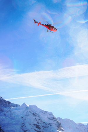 Red helicopter flying over Swiss Alpine mountain Mannlichen in winter, Switzerlandの写真素材