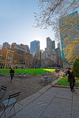 New York, USA - April 24, 2015: Tables and chairs and Skyscrapers viewed from Bryant Park in Midtown Manhattan, New York, NYC, the US. Tourists relaxing in the park. Selective focusのeditorial素材