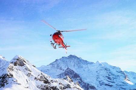 Maennlichen, Switzerland - December 31, 2013: Red helicopter flying near Swiss Alps mountain...
